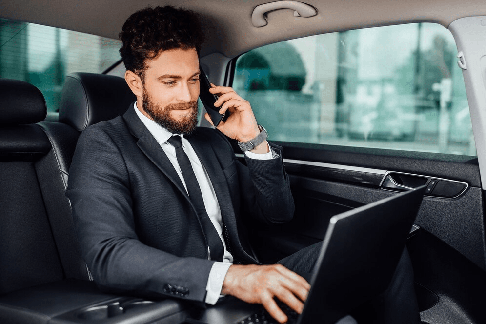 A Picture of a Business Man on the backseat of his car using his computer